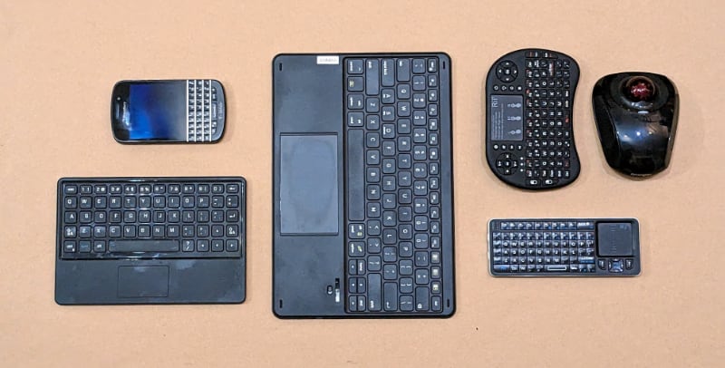 Finding a good, capable, and convenient remote for the smarter television project proved more difficult than I would have guessed. Here are things I tried (except for the BlackBerry phone at upper left, included for size comparison). Below the BlackBerry is the bluetooth keyboard from a BlackBerry Playbook keyboard case. Turns out, like everything from BlackBerry, it can't be used for anything except BlckBerry's now nonexistent services. In the center is an inexpensive bluetooth keyboard (that I thought would be the same size as the BlackBerry one. Oops). It worked somewhat, but its lack of mouse buttons was a fatal flaw. Next to it, at top, is the oddly shaped keyboard-trackpad that is my favorite, even though it doesn't work very well. To its right is a Kensington wireless mouse, that works well but has no keyboard. At bottom right is a cheap, tiny keyboard with trackpad that worked the best, but is inconvenient to hold and terrible for left-handers. (Credit: Dennis E. Powell)